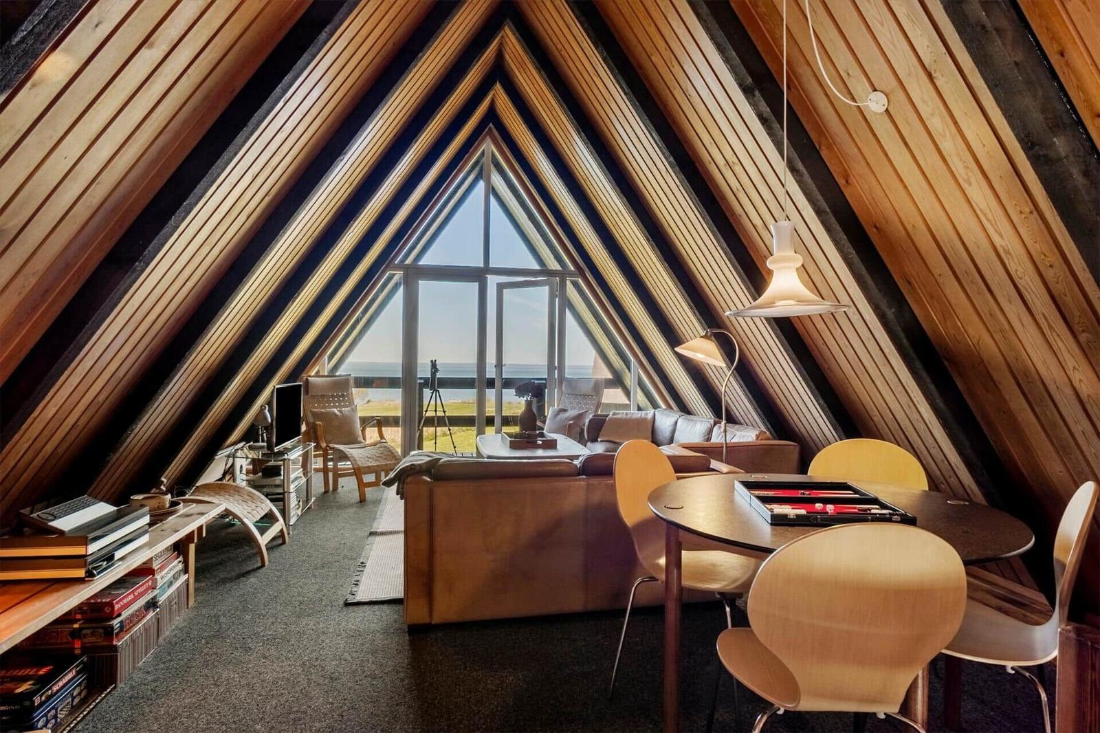 Wohnraum mit Holzdecke, Sofa, Tisch und Aussicht auf Meer.
