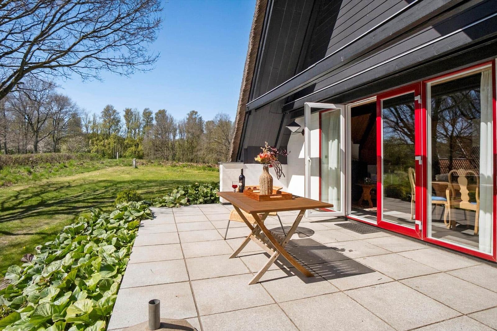 Terrasse mit Tisch und Stühlen, Blick auf grünen Garten und Wald.