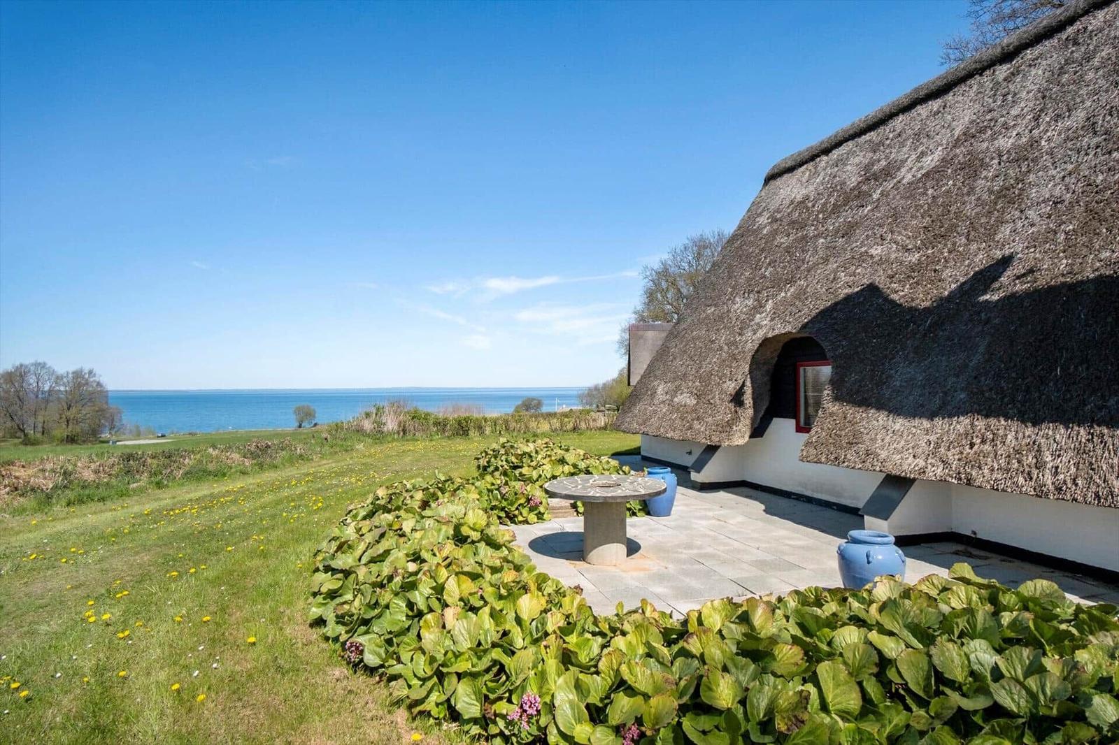 Haus mit Strohdach und Terrasse mit Blick auf Meer und Grünflächen.