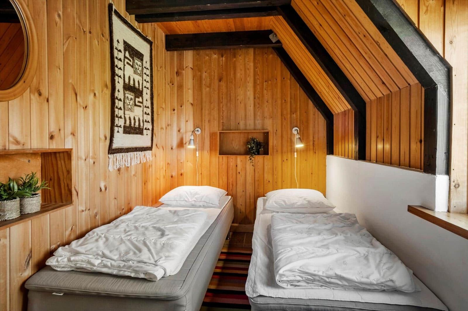 Zwei Betten in einem holzverkleideten Raum mit Dachschrägen und Wandlampen.