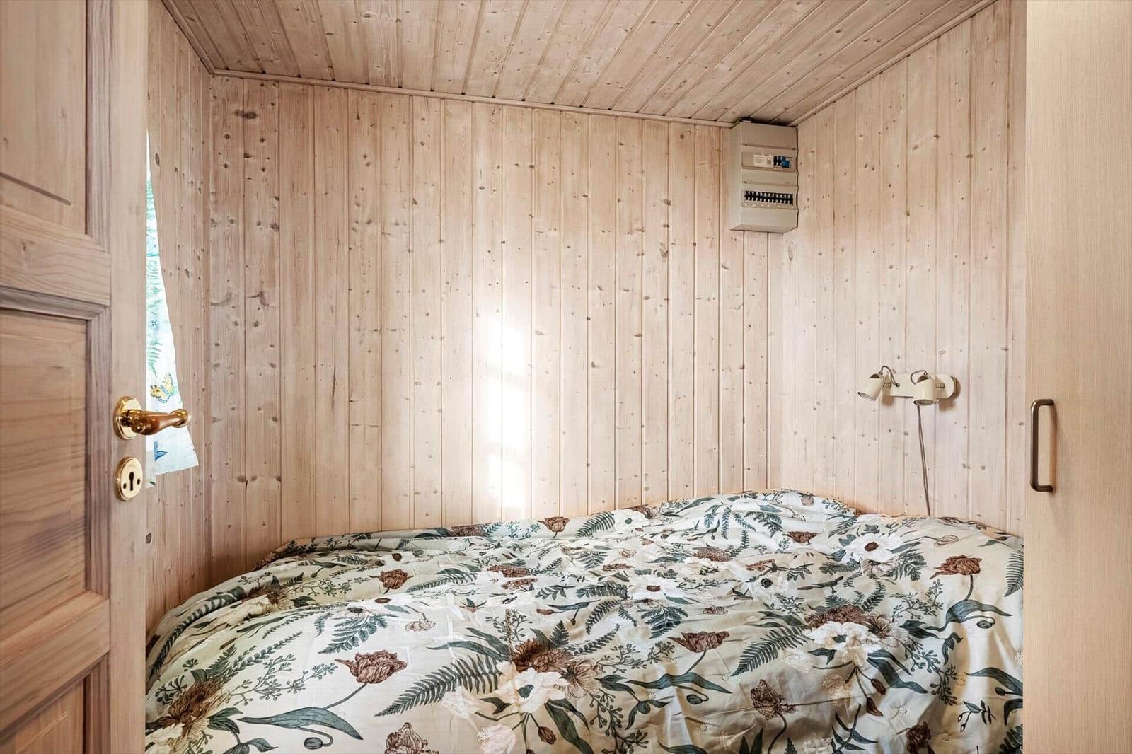 Bedroom with wooden walls, bed with floral bedding, and wall lamp.