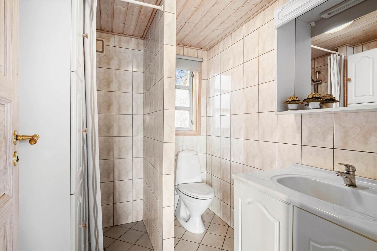 Bathroom with toilet, sink and shower. Wooden ceiling and tiled walls.