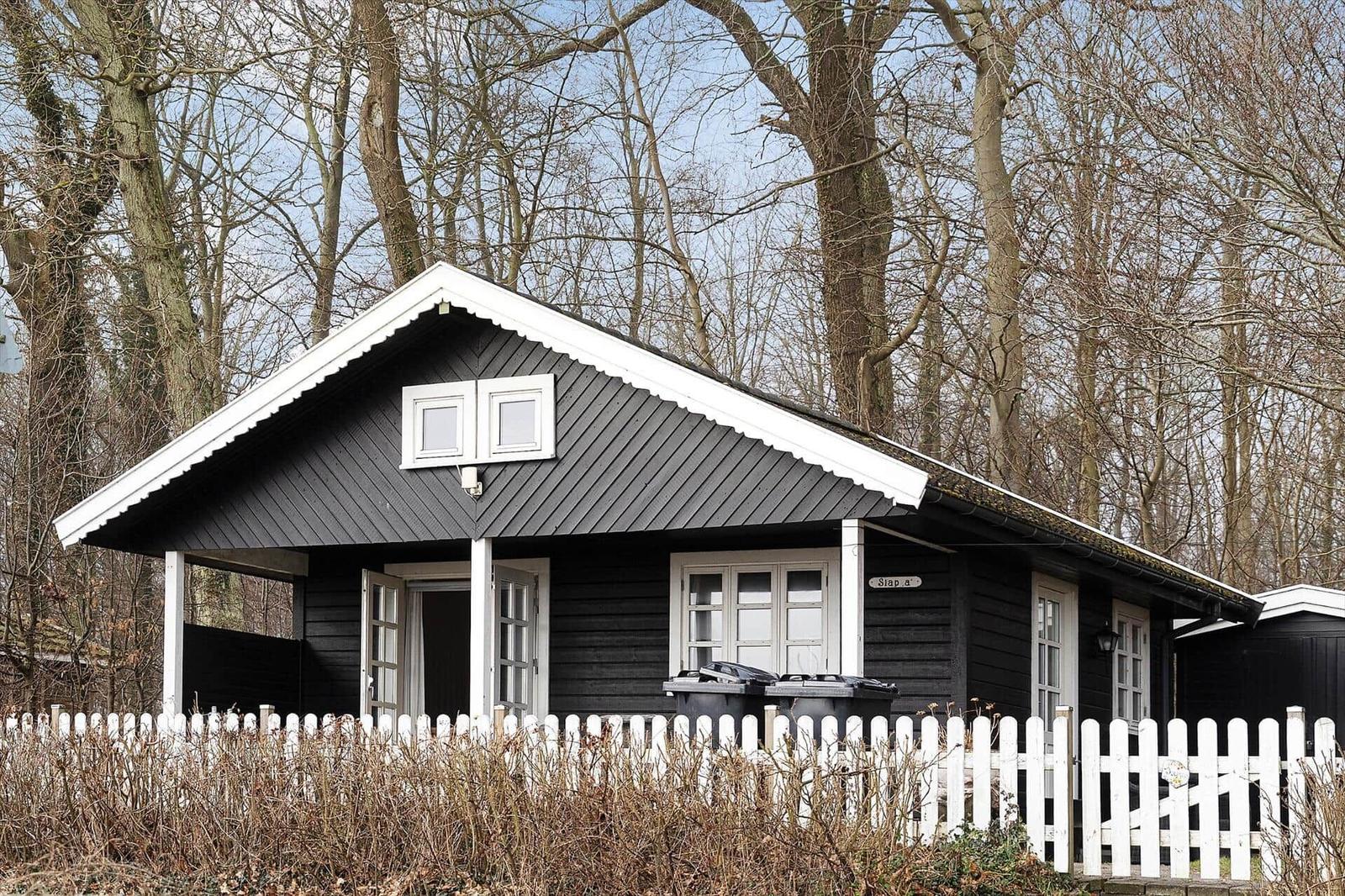 Black wooden house with white fence and windows in the woods.