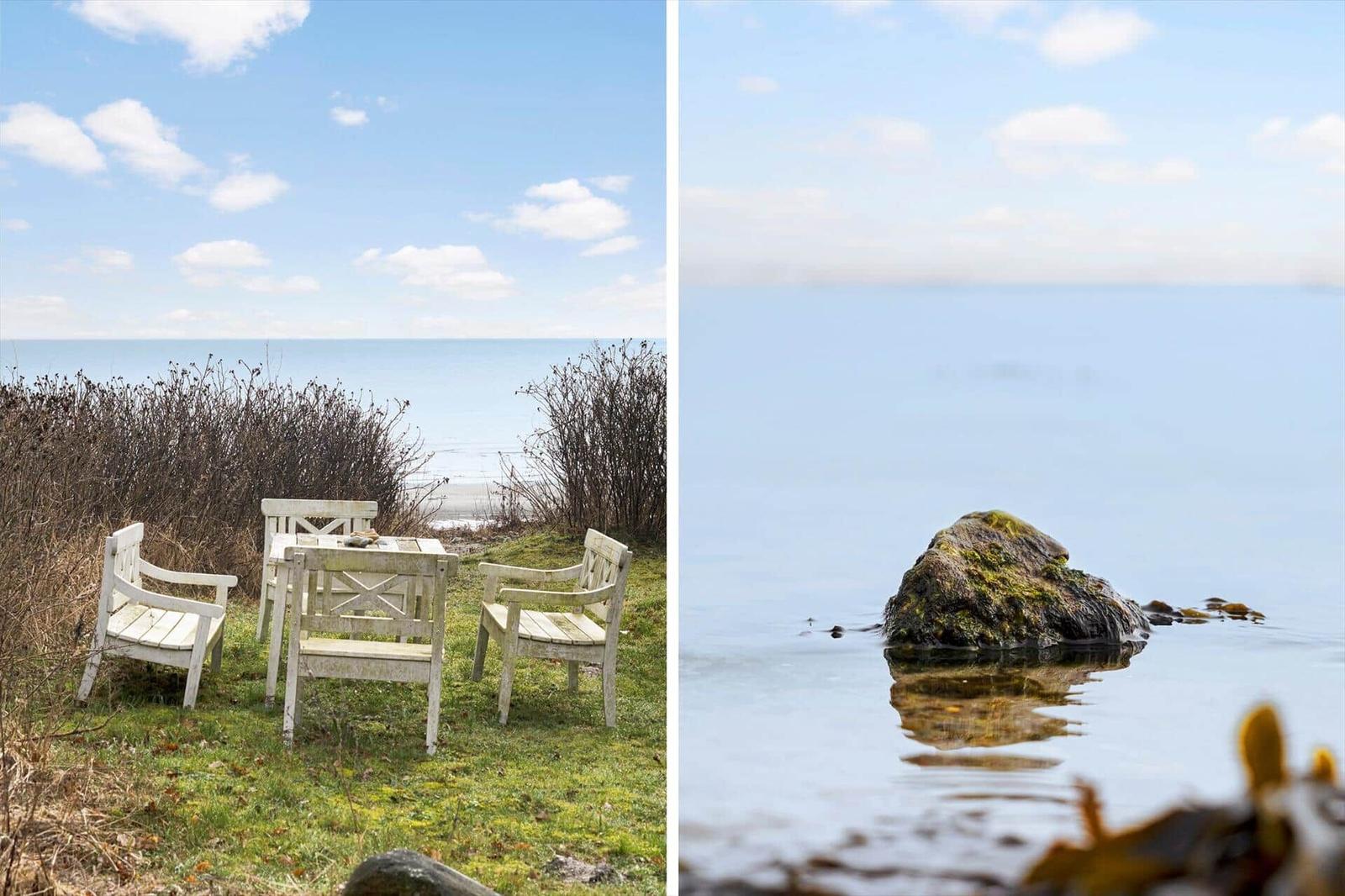 White garden furniture by the beach with a view of the sea. A large stone rises from the water.