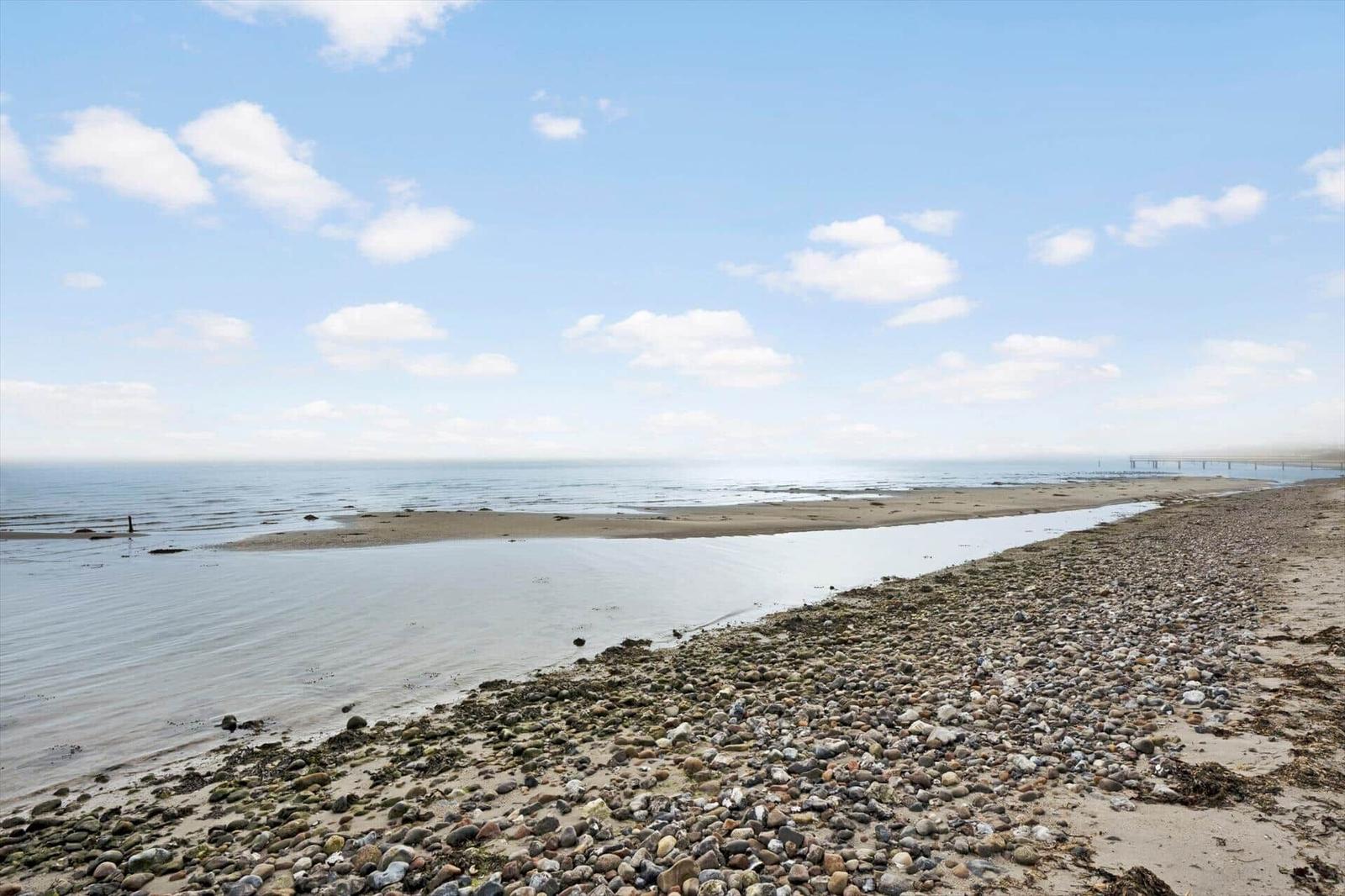 Rocky shore with water area and horizon under blue sky with white clouds.