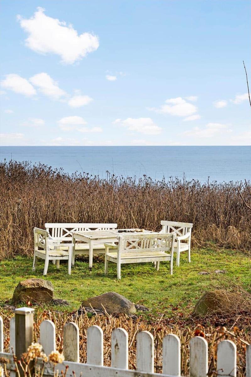 White garden furniture stands on a lawn facing the sea.