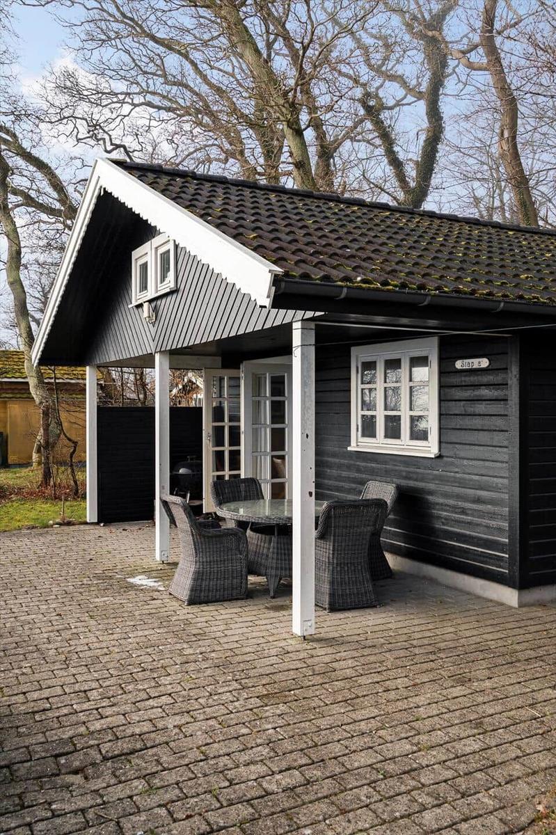 Black wooden house with terrace, table, and chairs under a roof.