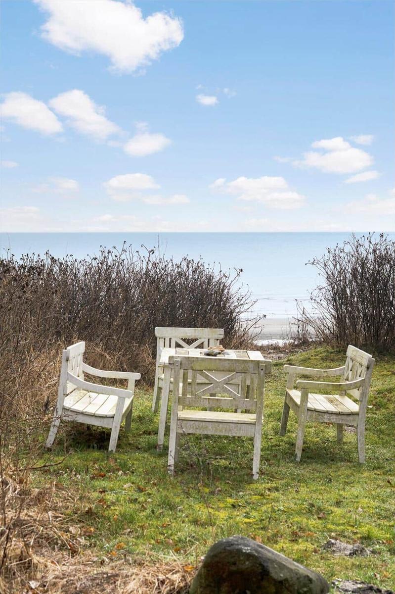 White wooden table and chairs on grass near beach and sea.