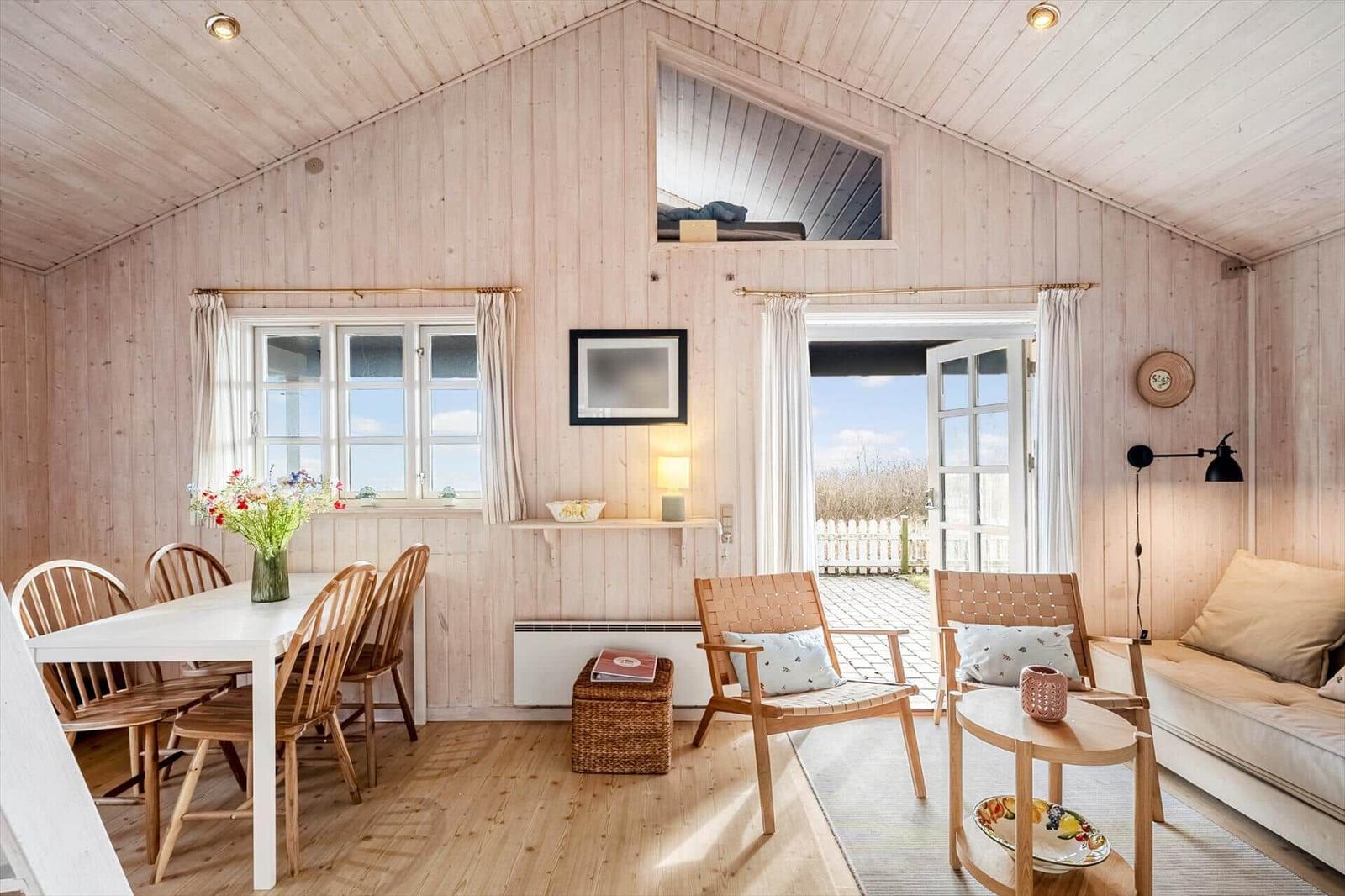 Living area with dining space, sofa, and loft bed. Wooden walls and floor.