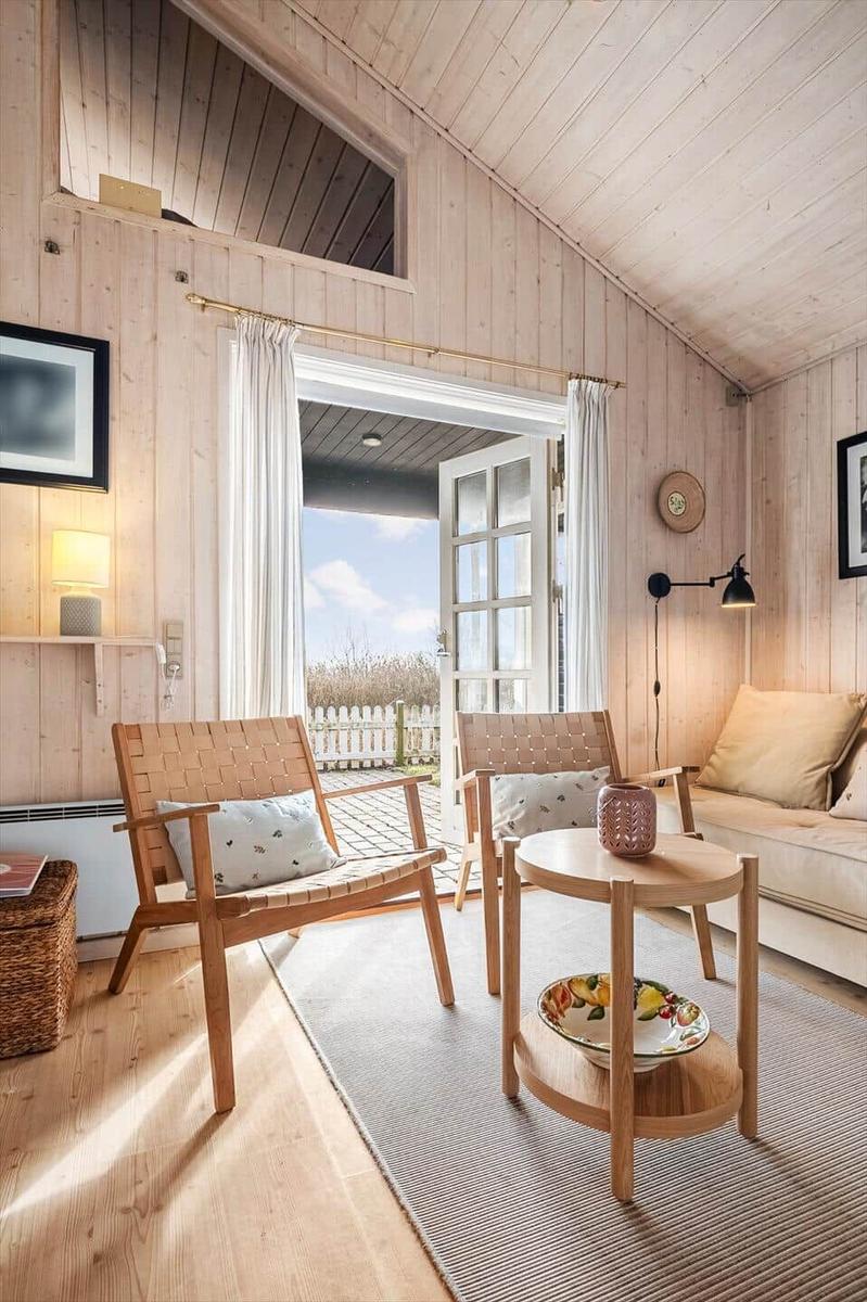 Living room with wood walls, two chairs, sofa, and table. Door leads outside.