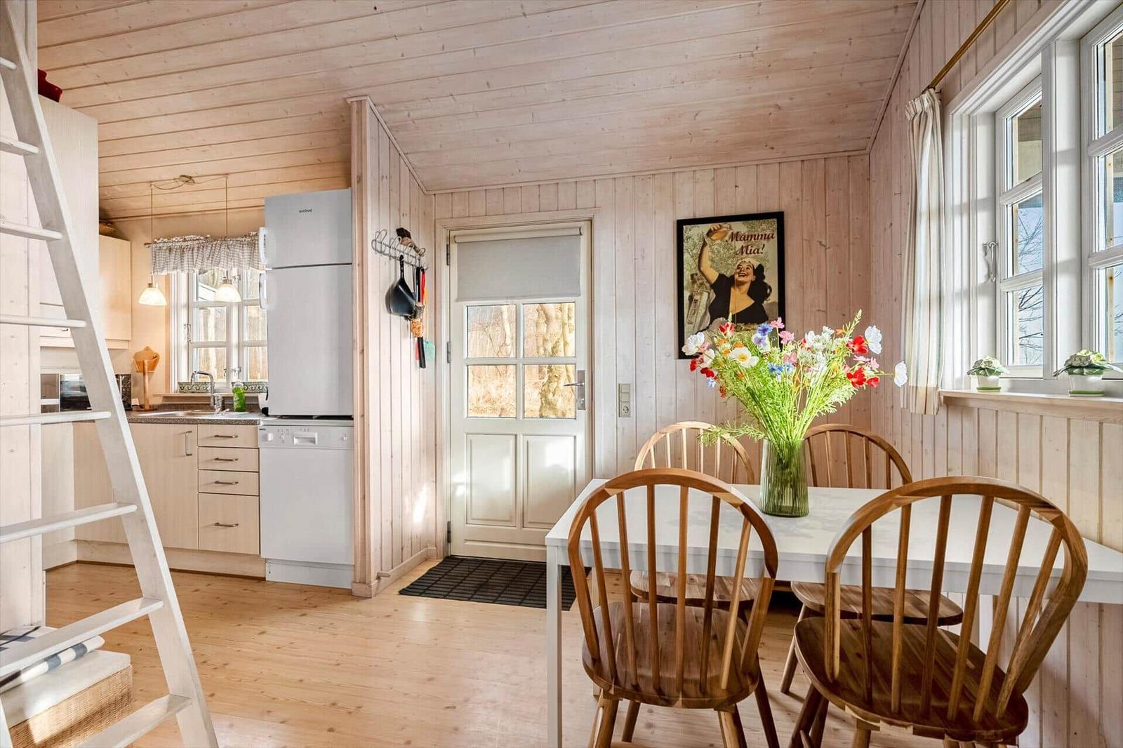 Kitchen and dining area with wooden walls, table, chairs, and windows.