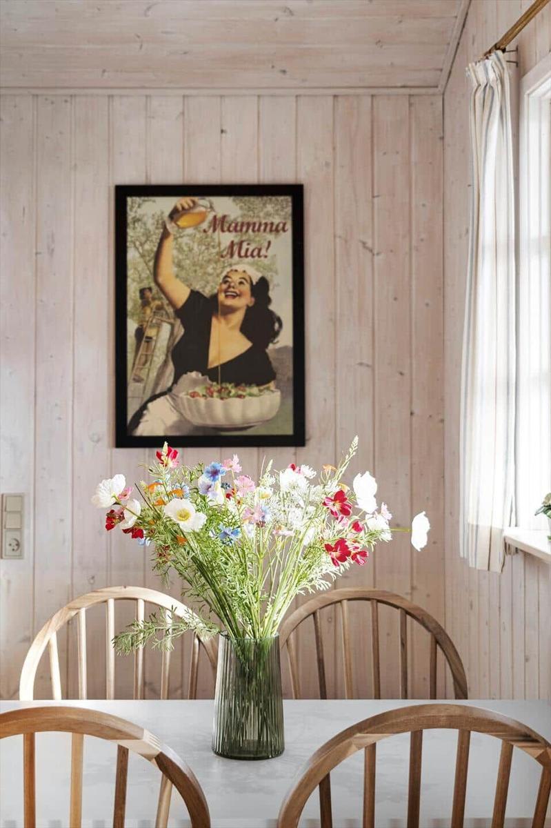 Dining room with wooden walls, table, chairs, and flower bouquet. Wall poster with Mamma Mia!