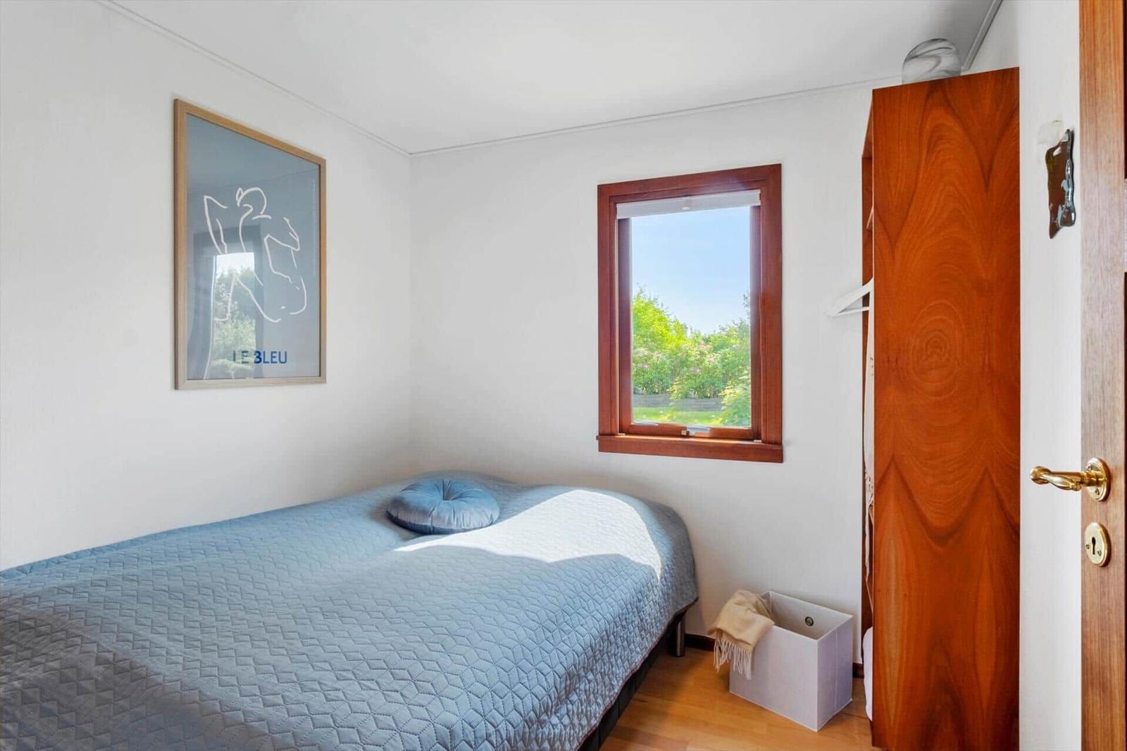 Schlafzimmer mit Bett, Fenster und Holzschränkchen