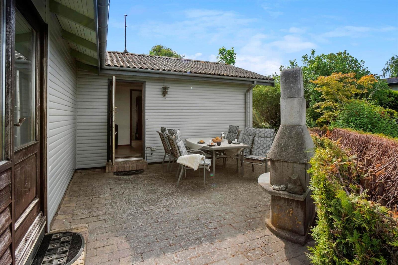 Terrasse mit Tisch, Stühlen und Grill. Hinterhof mit Beerensträuchern und Bäumen.