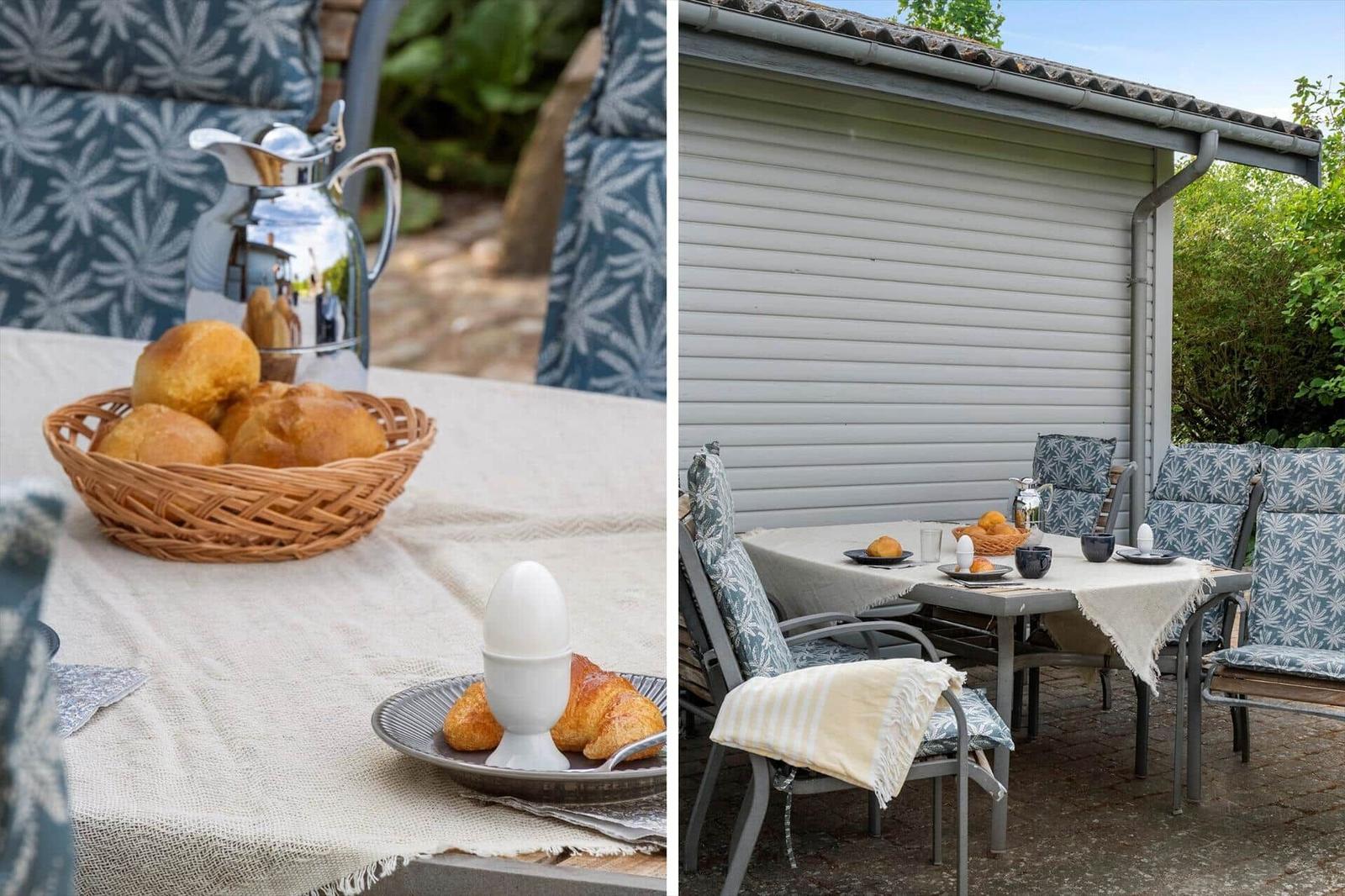 Außentisch mit Korb, Brötchen und Kaffeekanne. Sitzgruppe mit blau gemusterten Kissen.