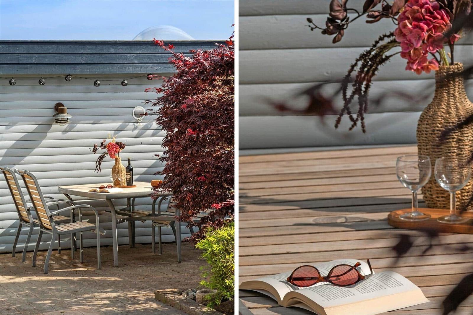 Terrasse mit Tisch, Stühlen und Blumen. Holztisch mit Buch und Sonnenbrille.