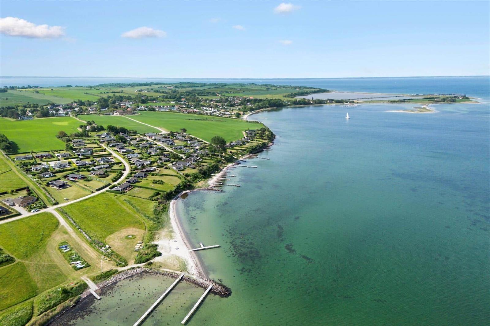 Aerielansicht einer Küstenlandschaft mit Häusern, grünen Feldern und einem Boot im Wasser.