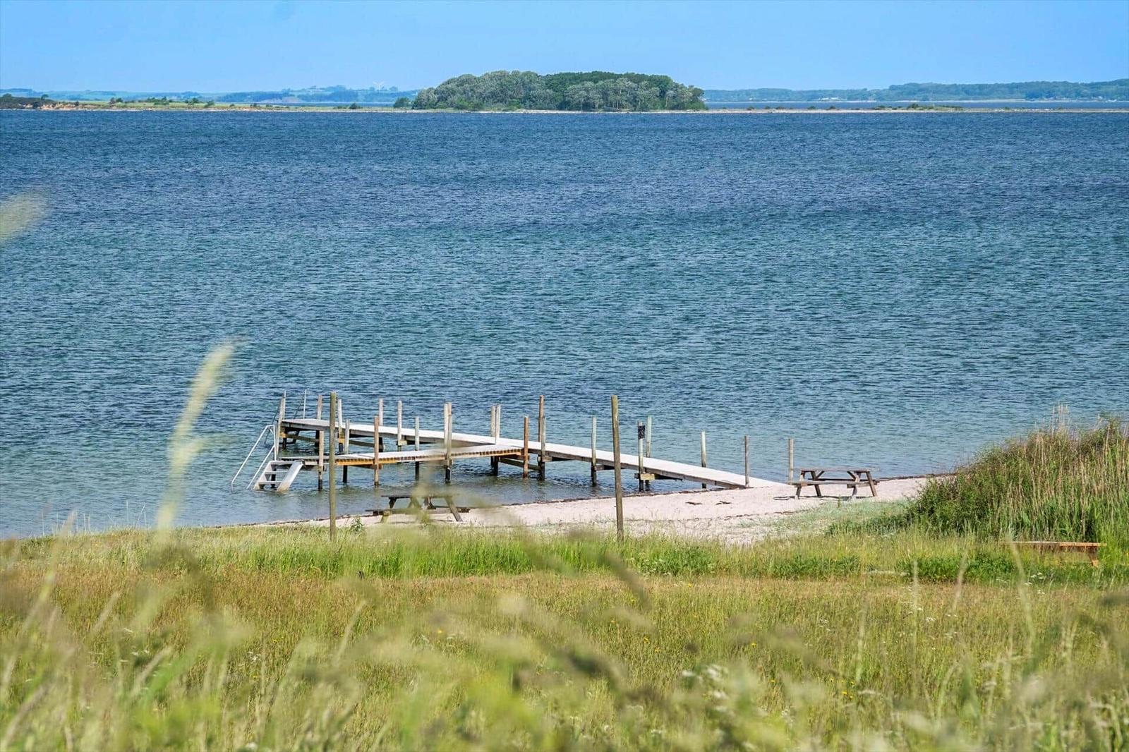 Holzsteg führt zum Wasser. Picknicktisch und Strand im Vordergrund.