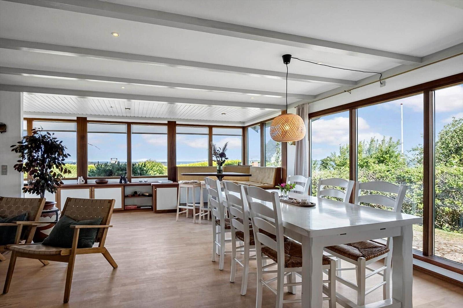 Esszimmer mit weißem Tisch und Stühlen, großes Fenster mit Blick auf die Landschaft.
