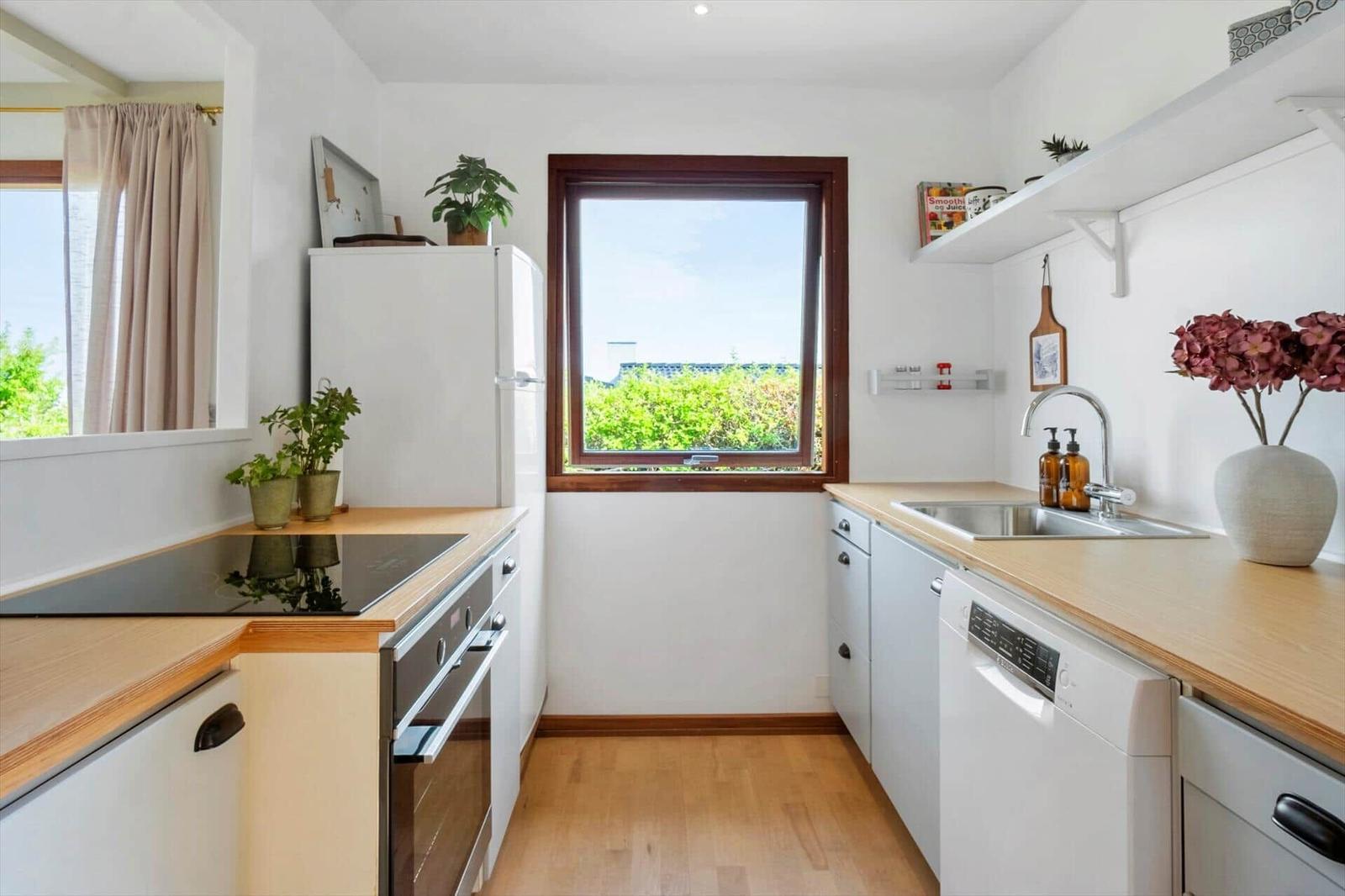 Küche mit Holzoberflächen, weißer Einbauküche und Fenster mit Blick auf Grün.