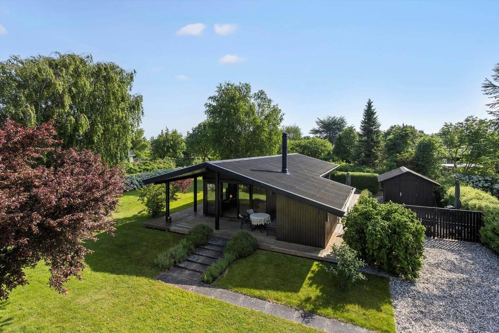 Modern wooden cabin with terrace and garden. Grill hut and green surroundings.