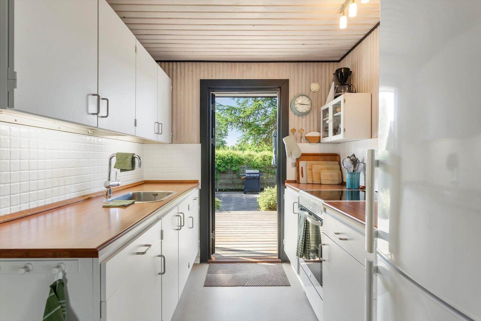 Kitchen with wooden countertops, white cabinets, and door to the garden.