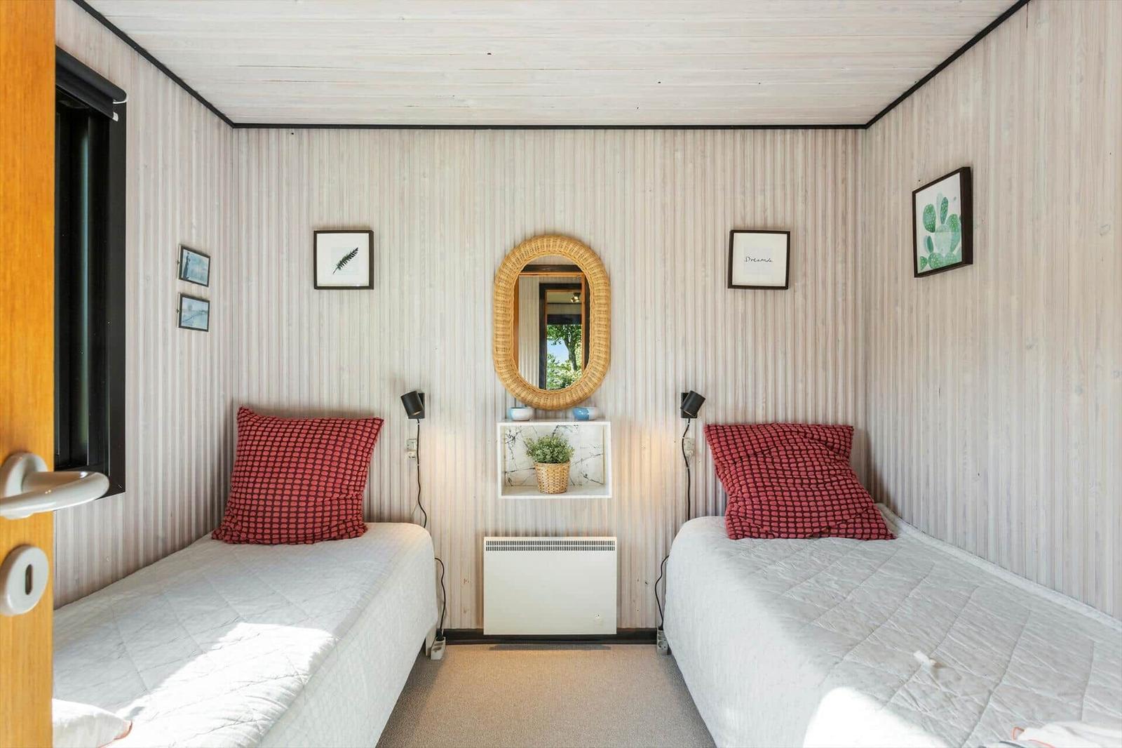 Two beds with red pillows, wall mirror, and plant in the room.
