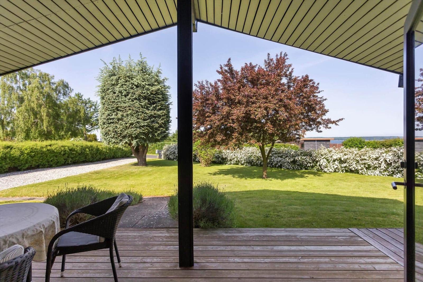 Deck with seating and view of garden with trees and lawn.
