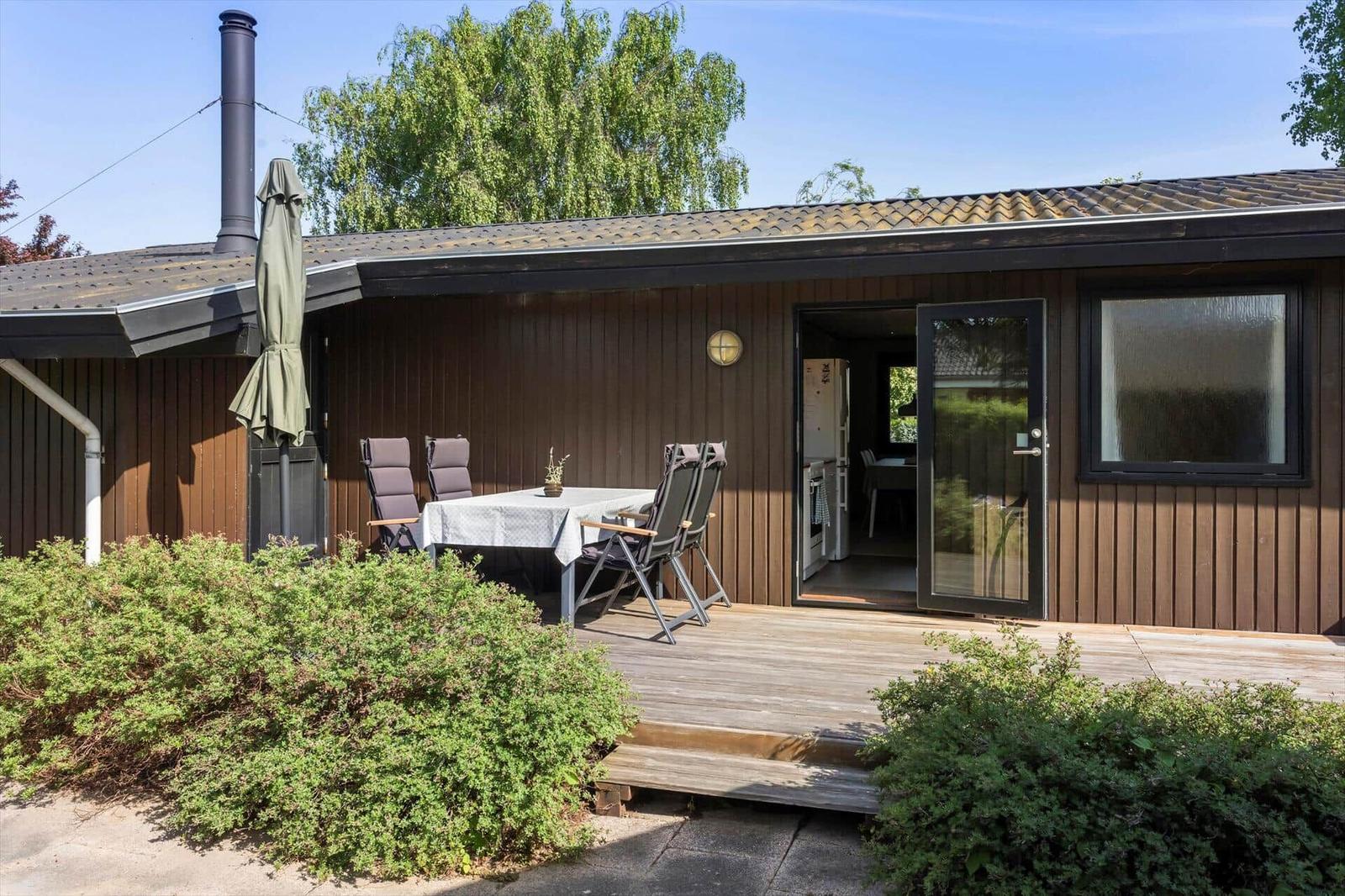 Wooden deck with table and chairs in front of a house with an open door.