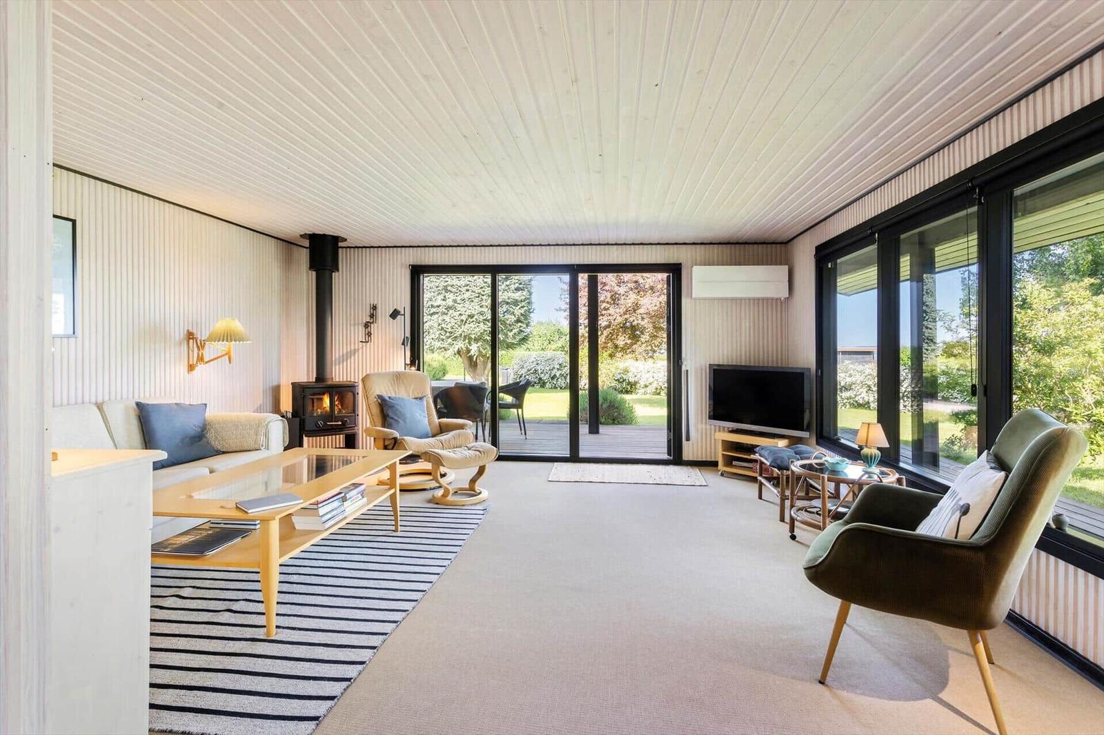 Living room with sofa, armchairs, and fireplace. Large windows offer garden view.