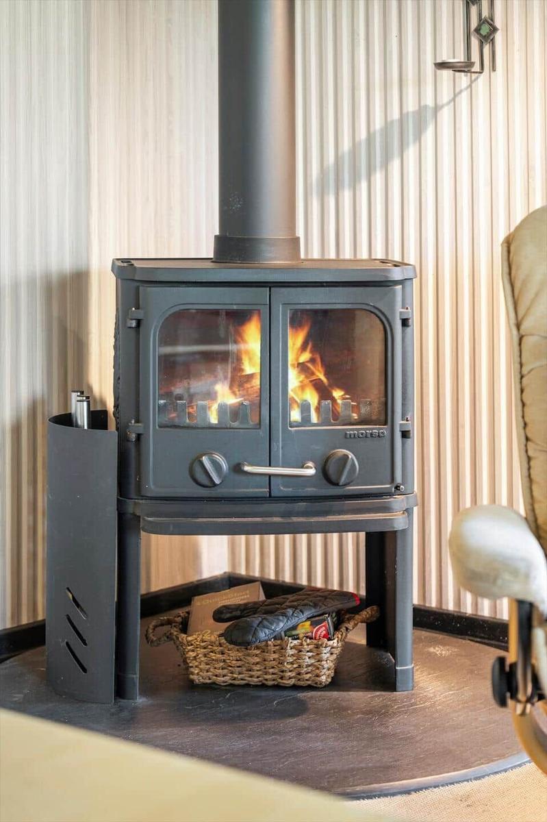 A wood stove with burning fire and a basket with accessories underneath.