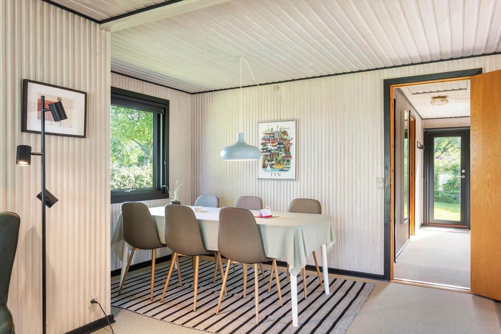 Dining room with table, chairs, and window. Wall cladding and ceiling visible.