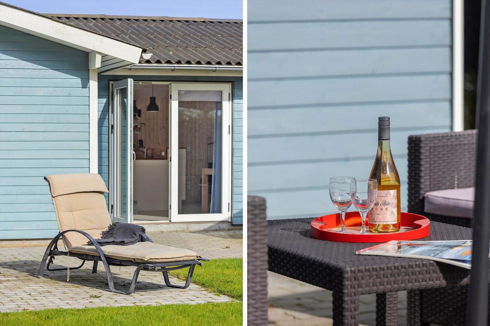 Outdoor area with lounge chair and table with wine and glasses in front of a light blue house.