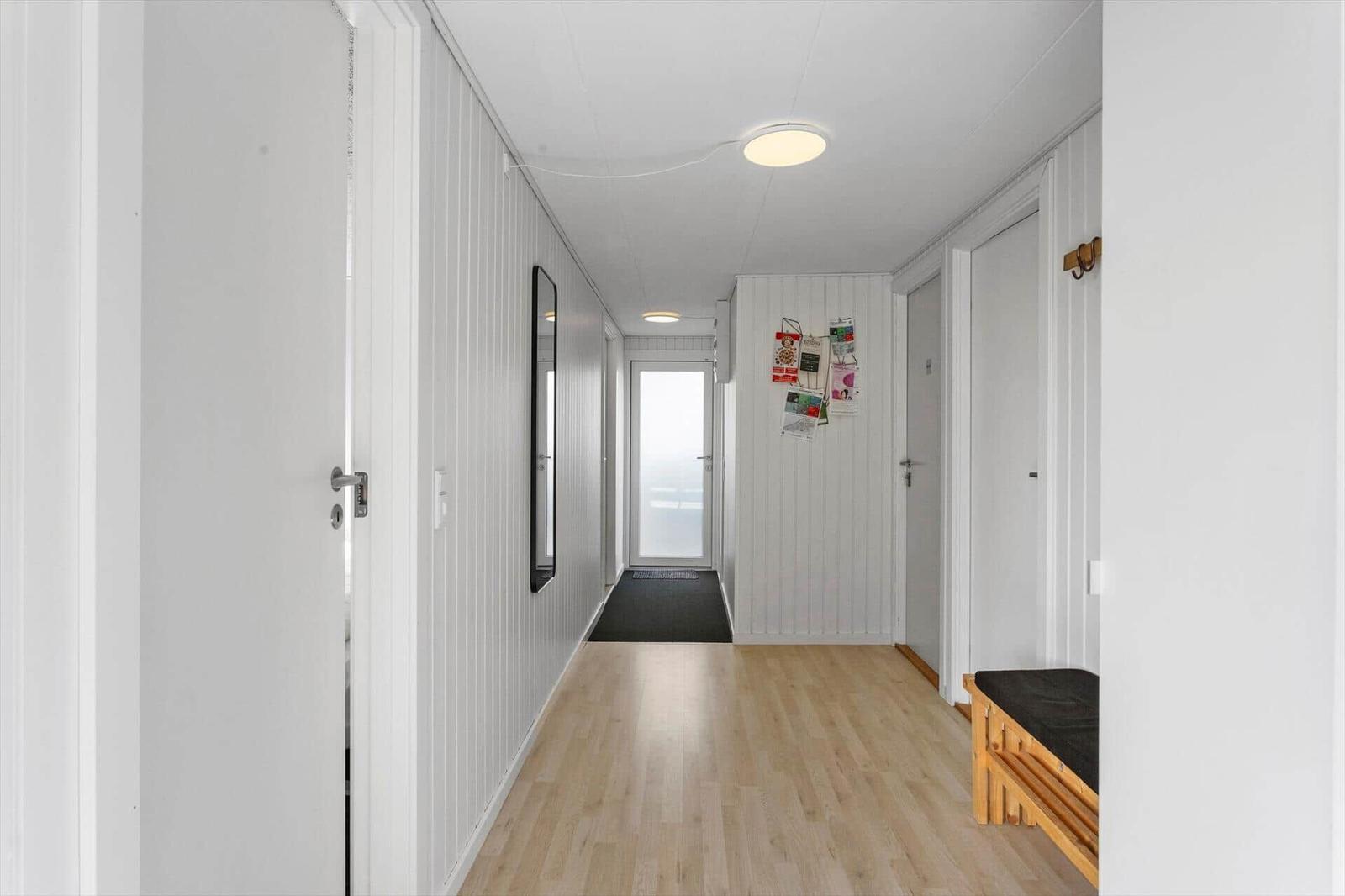 Hallway with wooden floor, white walls and doors. A mirror and a bench with seat are on the wall.