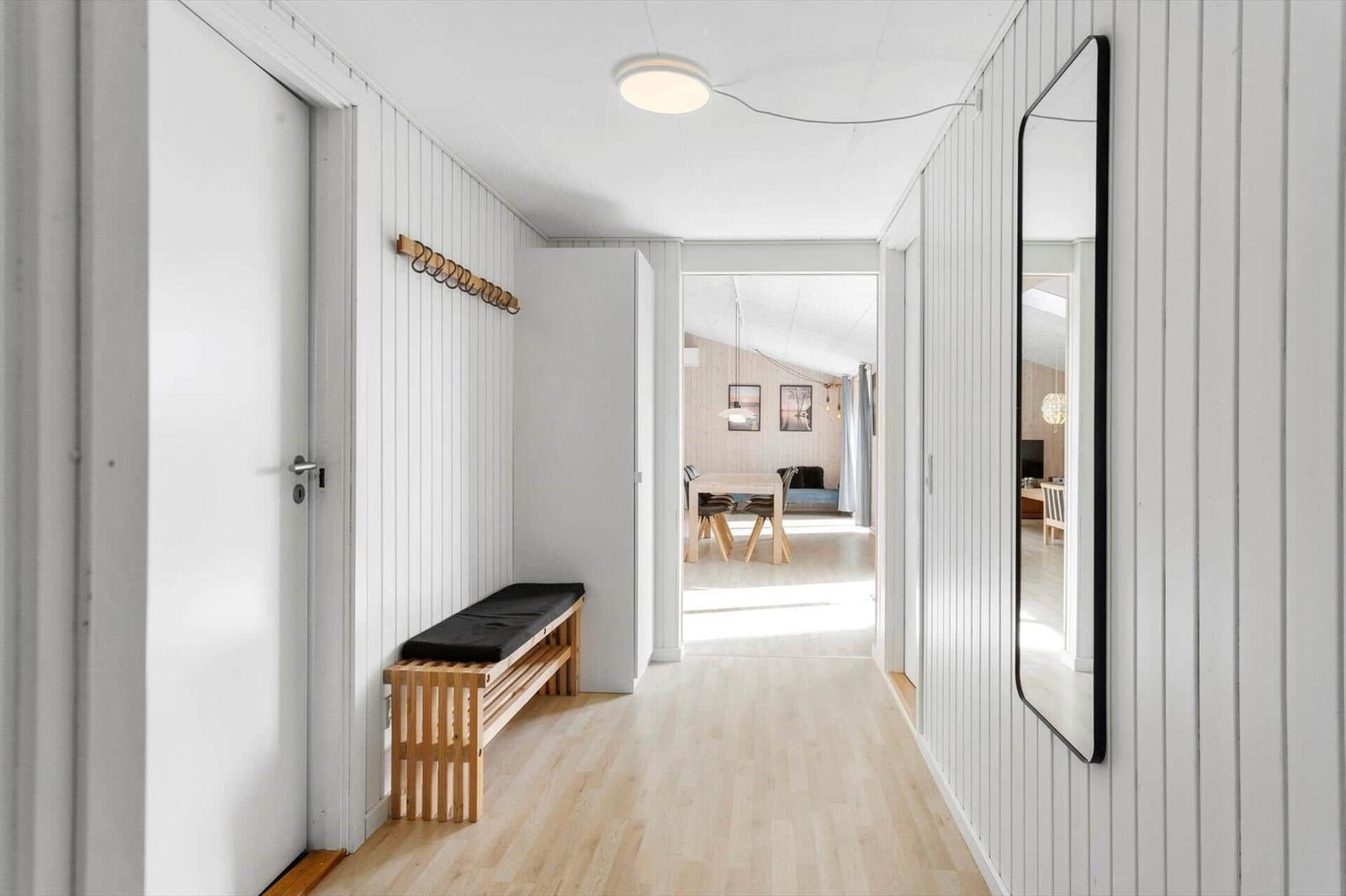 Hallway with wooden floor, wall mirror, and bench with seat cushion. Passage to dining area.