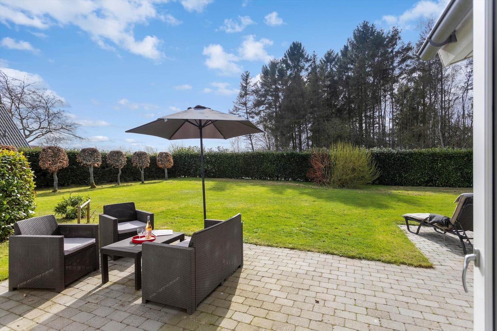 Terrace with seating group, umbrella, and garden. Backyard with lawn and hedge.