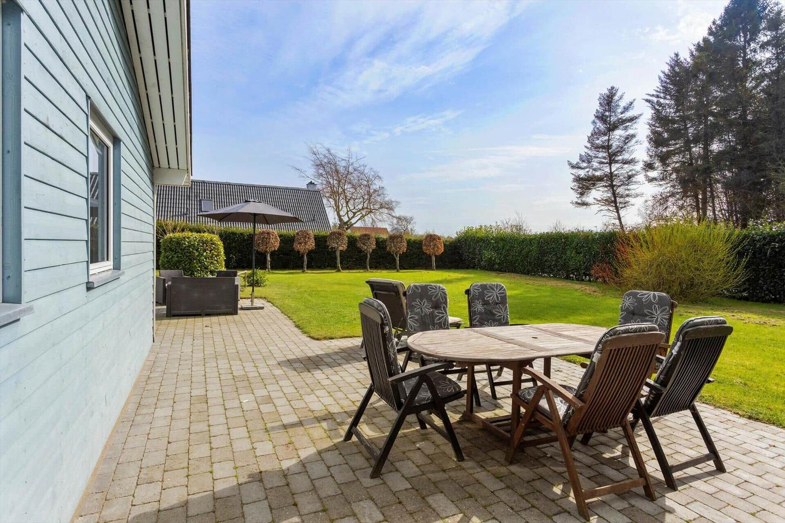 Patio with table and chairs, lawn area, and trees in the background.