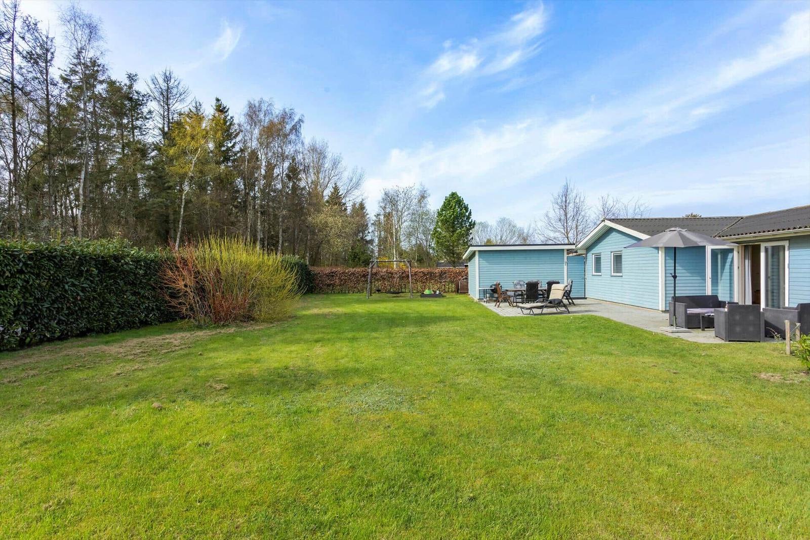 House with garden, terrace, and garden furniture. Background: forest and hedge.