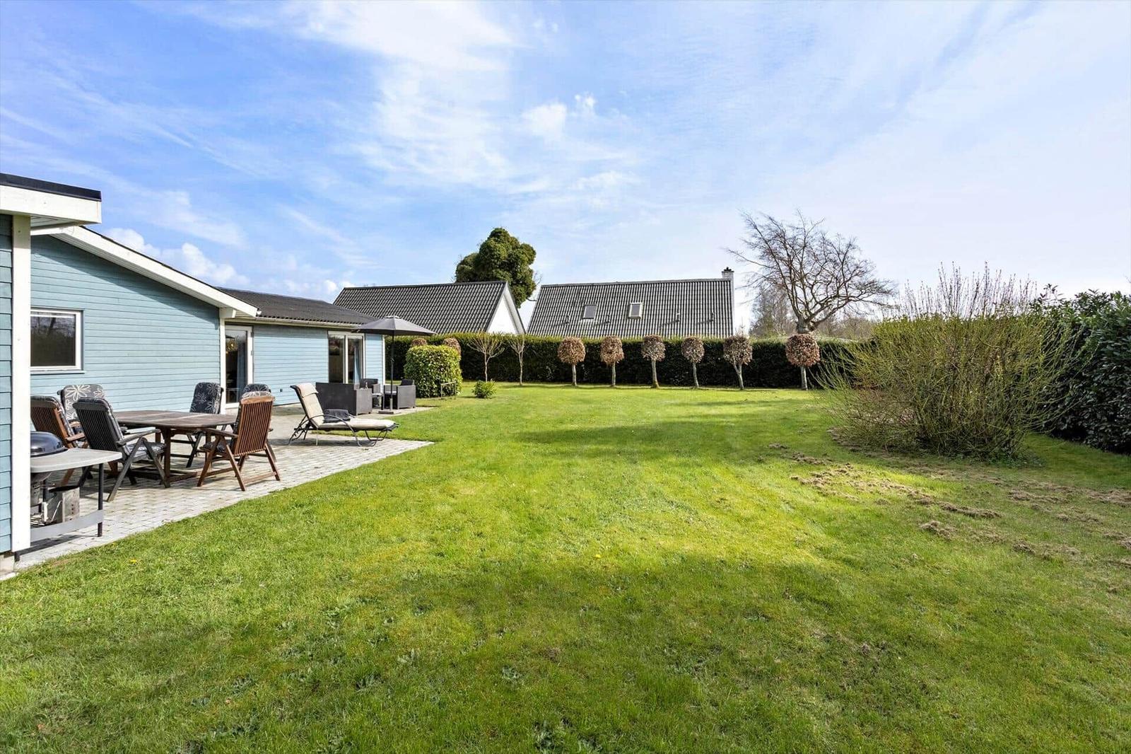 Backyard with lawn, patio, and garden furniture. Houses and trees are visible in the background.