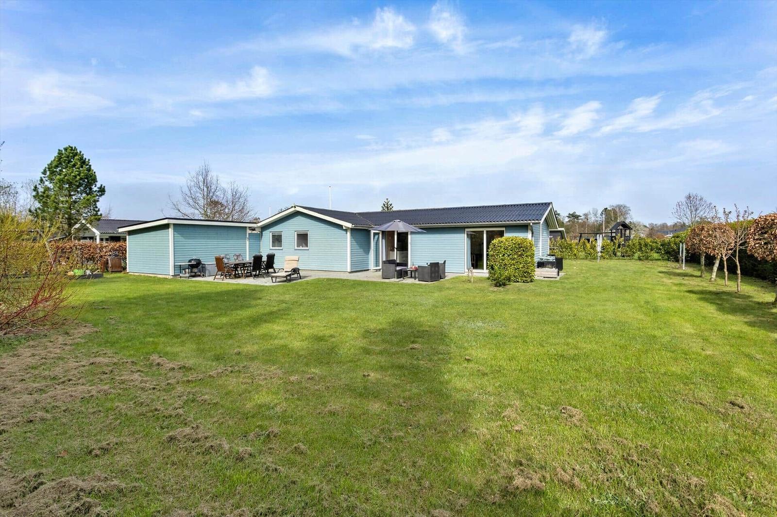 A light blue holiday home with terrace and garden under a blue sky.