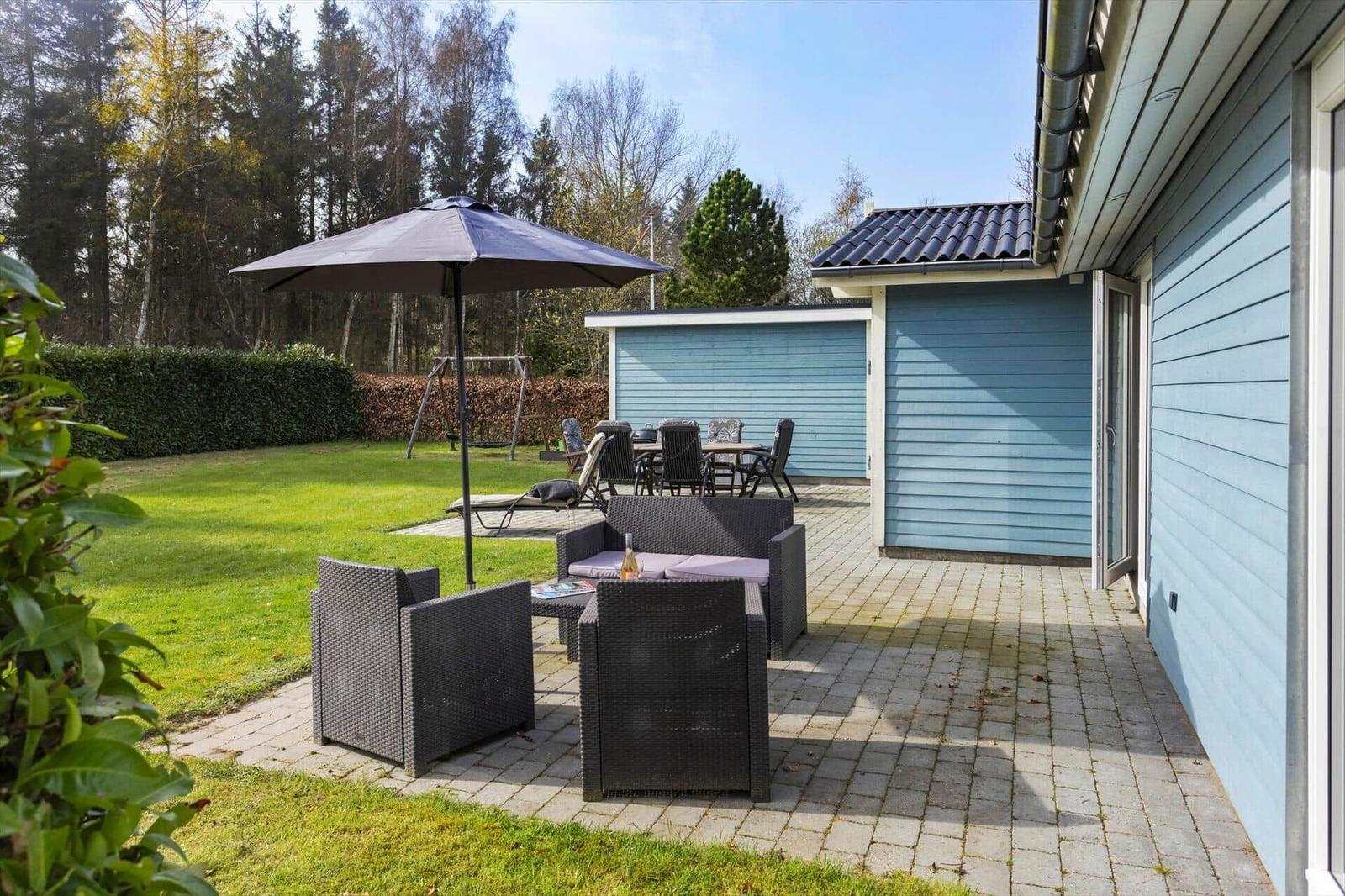 Terrace with seating area, umbrella, and garden space beside a blue house.