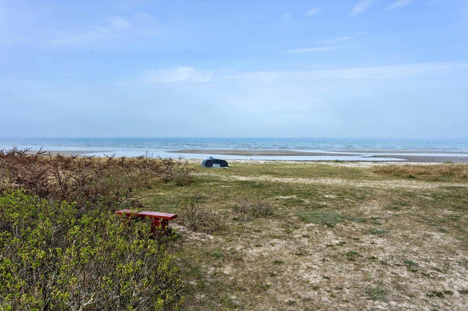 Red bench beside shrubs, view of beach and sea