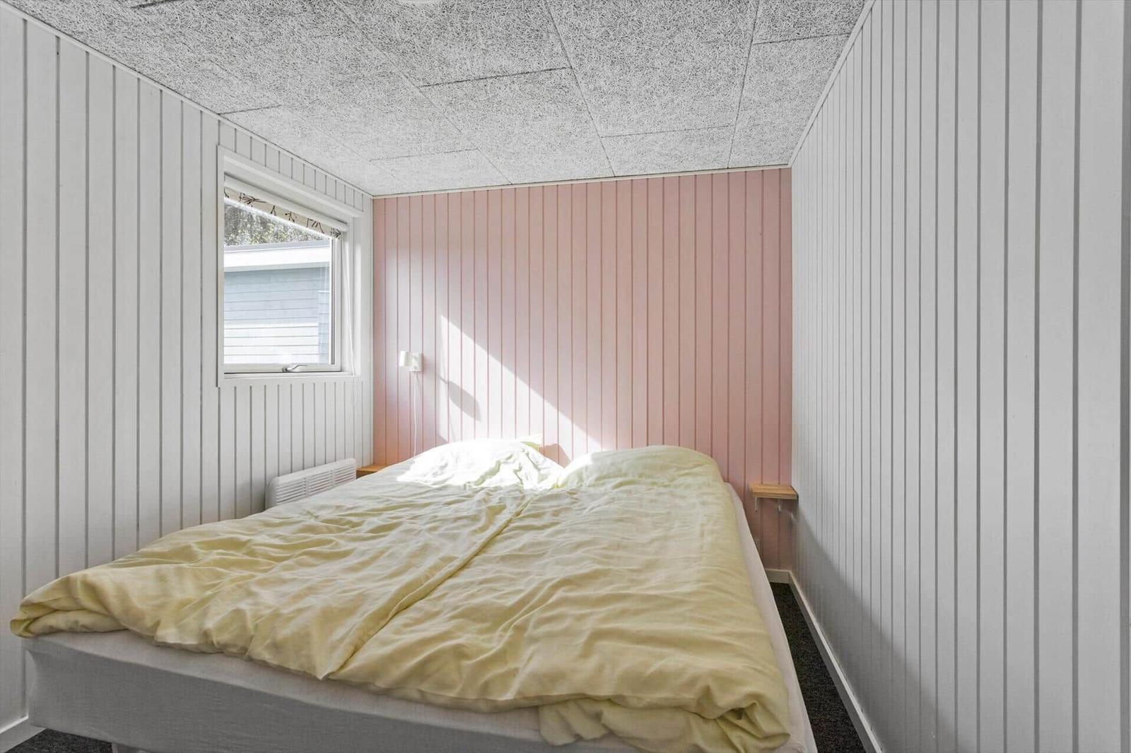 Bedroom with bed, window, and pink wall paneling.