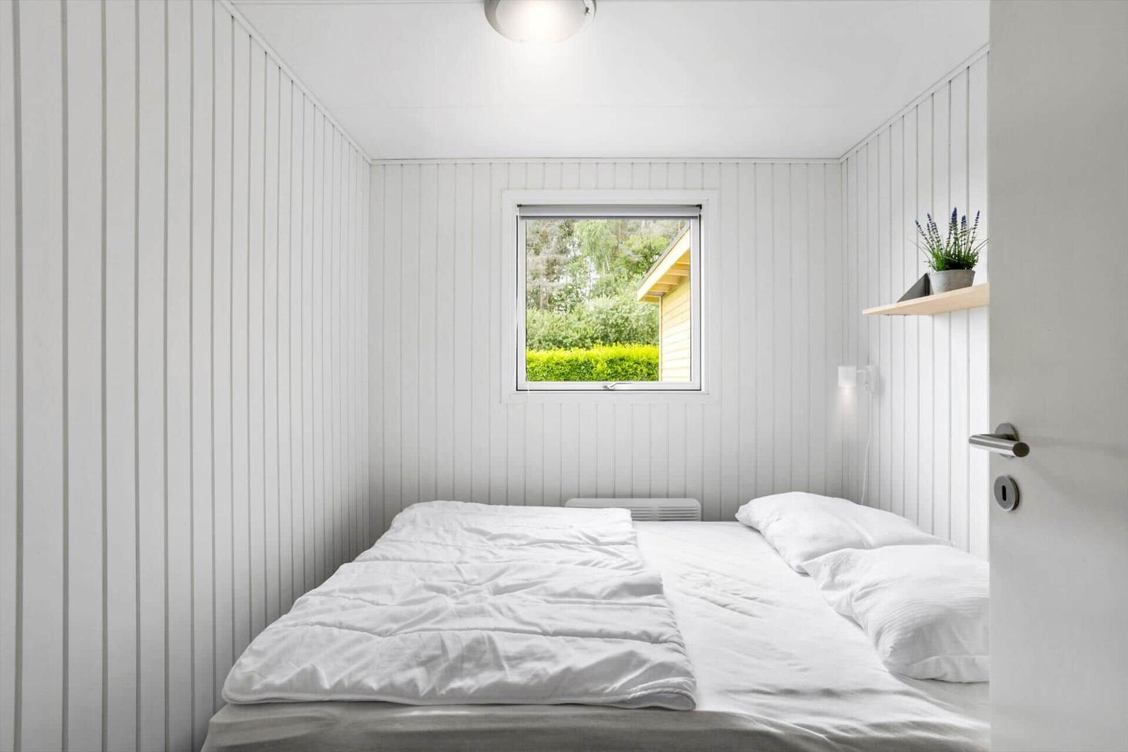 Bedroom with white bedding, window, and wood paneling.