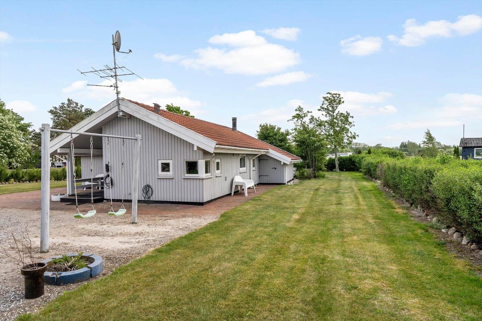 Ein Ferienhaus mit Garten, Schaukel und Terrasse unter blauem Himmel.