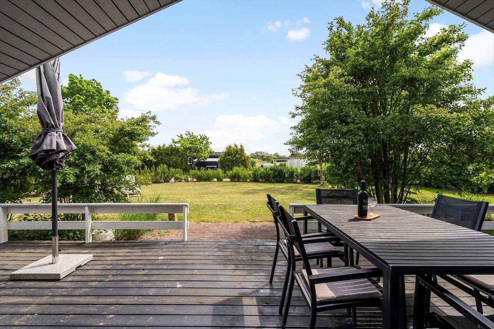Terrasse mit Tisch und Stühlen, Blick auf Grünfläche und Bäume unter blauem Himmel.