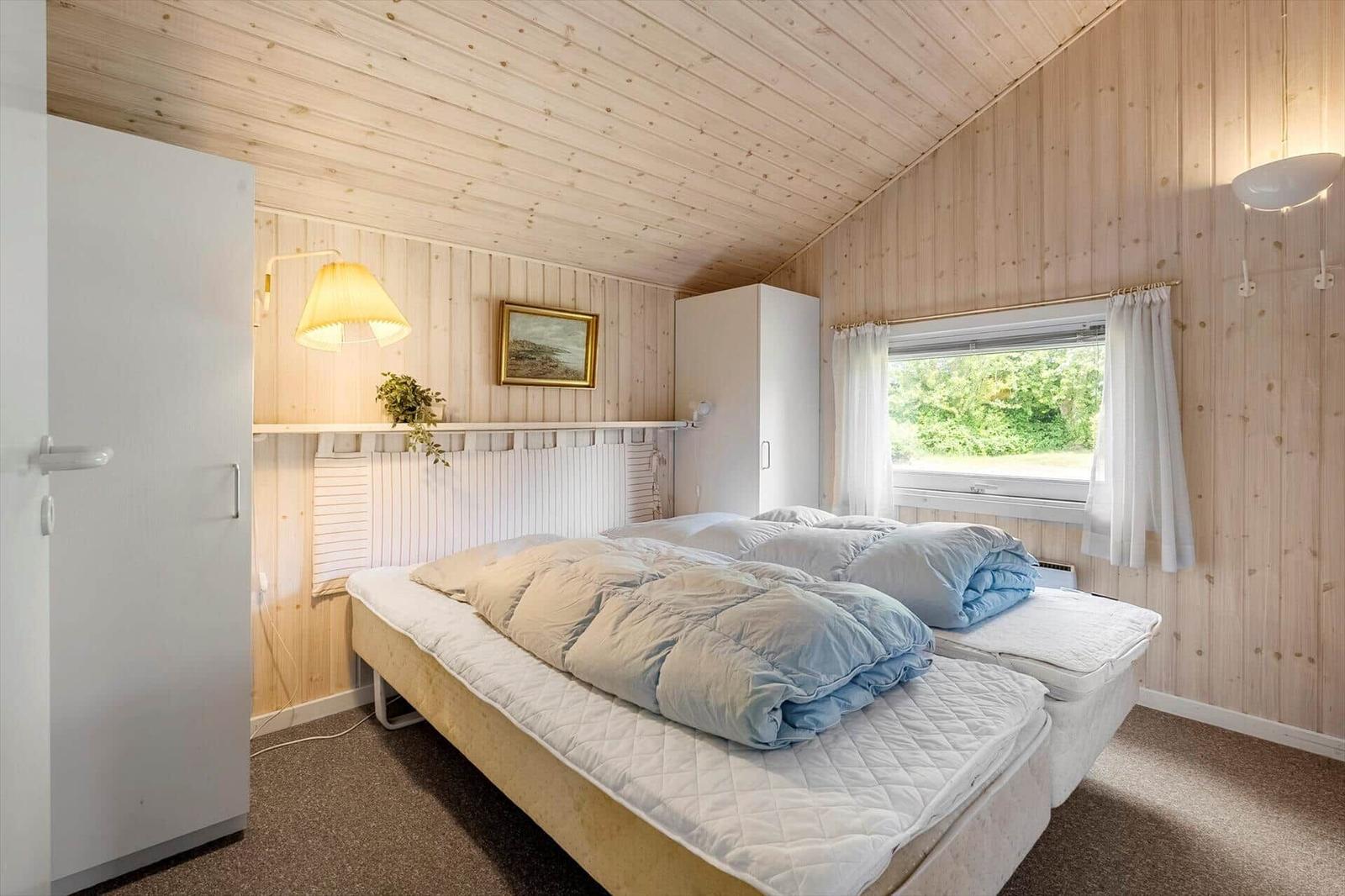Schlafzimmer mit Holzwand, Bett, Fenster und Schrank.