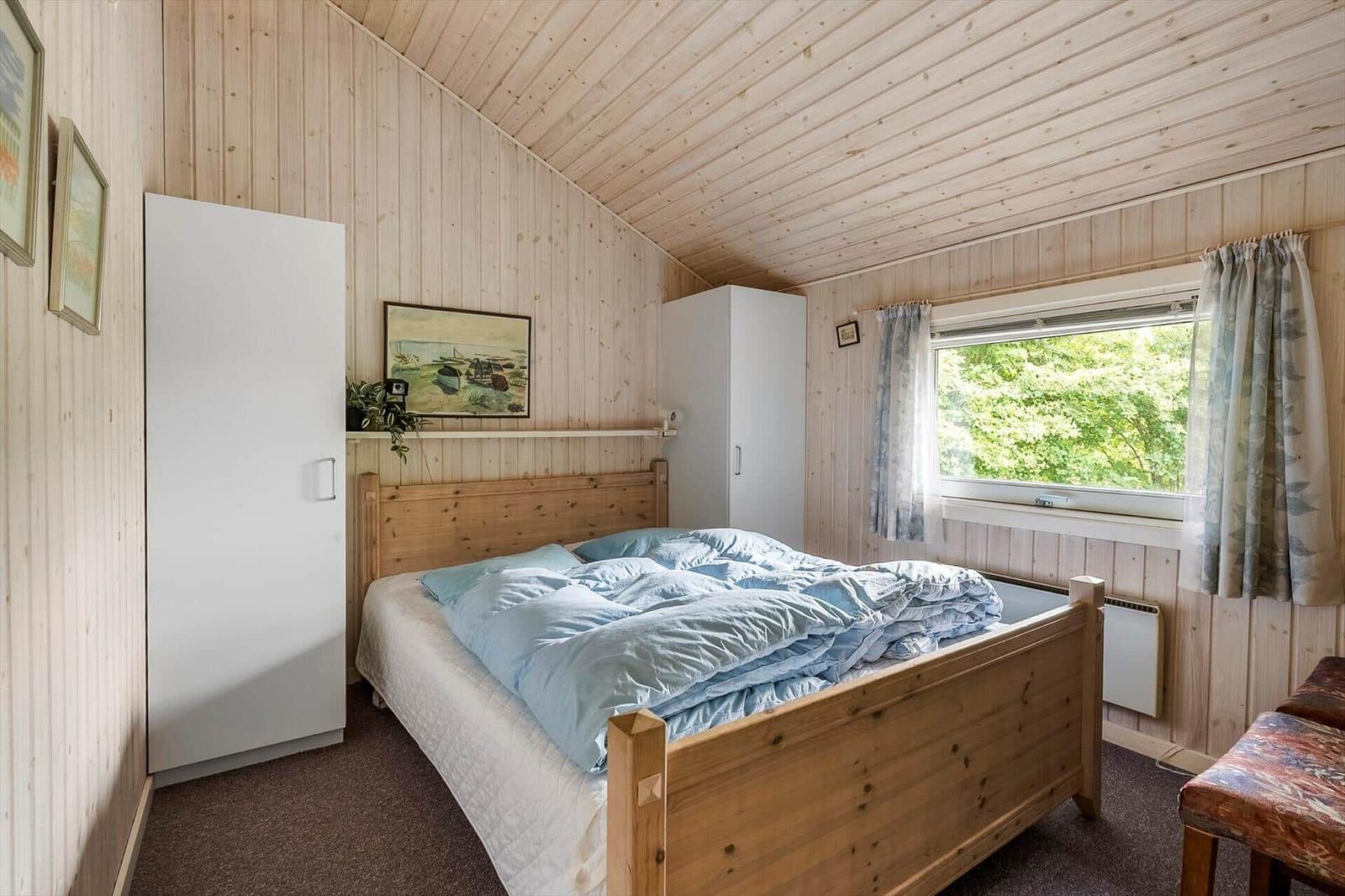 Schlafzimmer mit Holzwand, Bett, Fenster und Schränken.