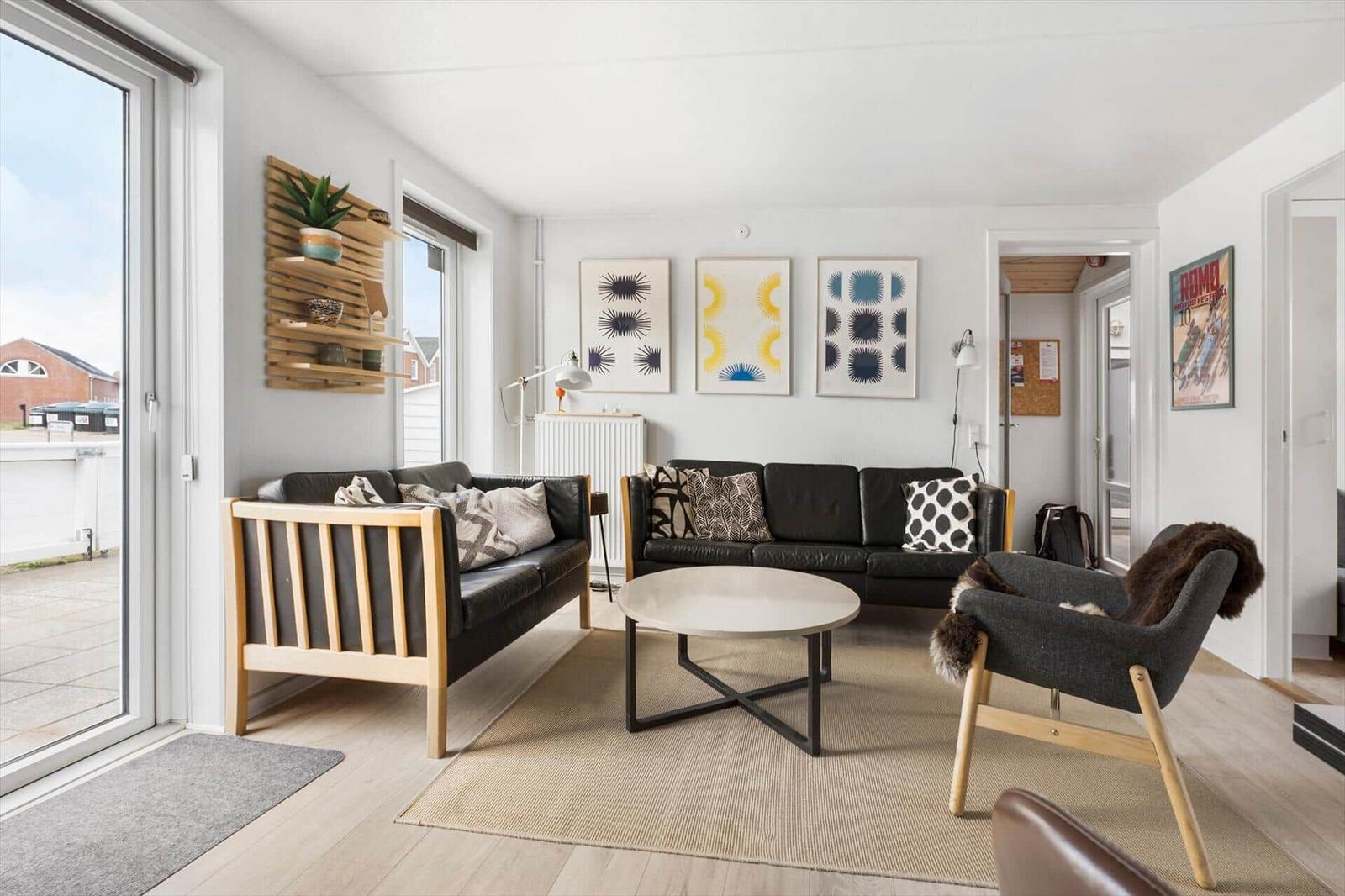 Wohnzimmer mit zwei Sofas, runden Tisch und Wandbildern. Terrassentür führt nach draußen.