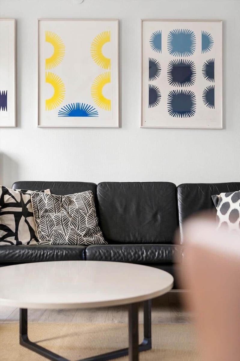 Schwarzes Sofa mit Kissen, runder Tisch und Wandbilder mit geometrischen Mustern.